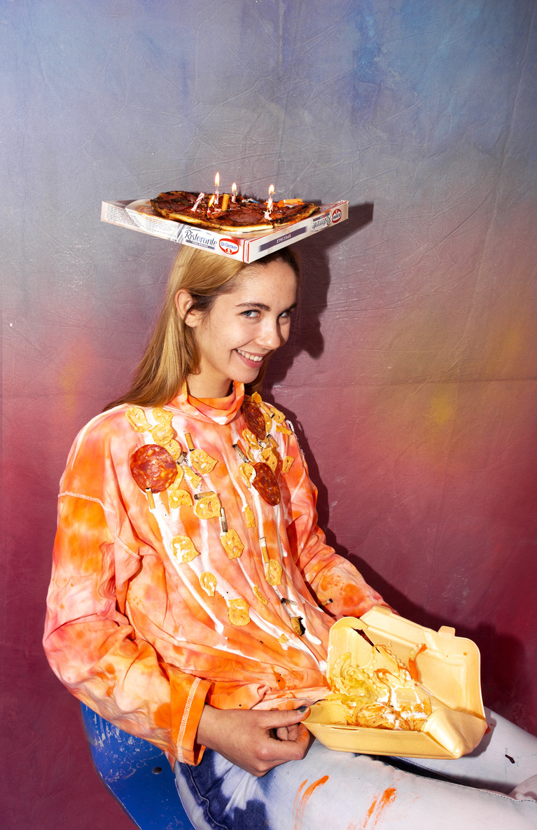 Une jeune femme avec un carton de pizza sur la tête qui tient un emballage de Kebab