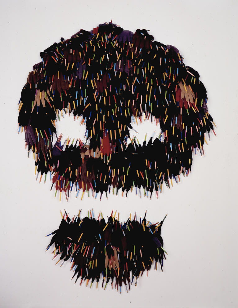 Une oeuvre en forme de crâne, constituée de gants et crayons de couleur.