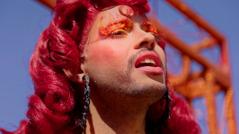 Brandon Gercara, in a red wig, is performing on a red sparkly stage.